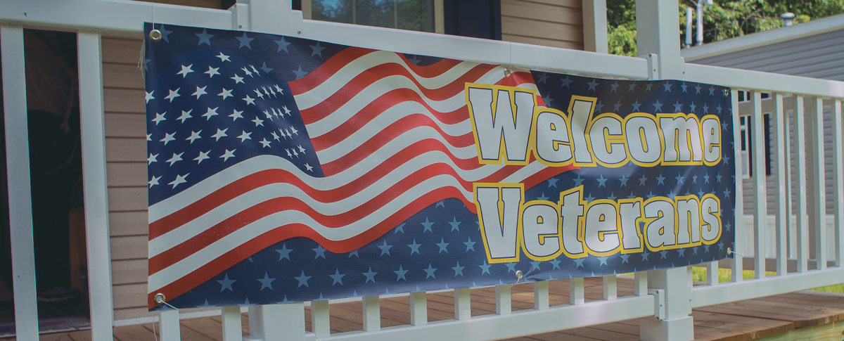 Photo of a banner hanging on a front porch that reads "Welcome Veterans" and has an American flag on it.