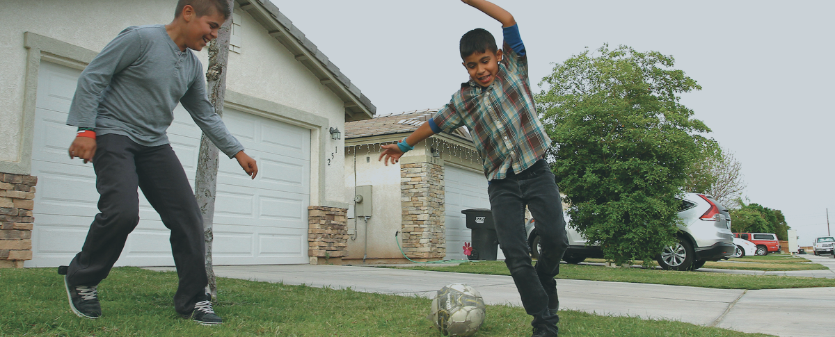 Photo of two boys playing soccer in their front yard.
